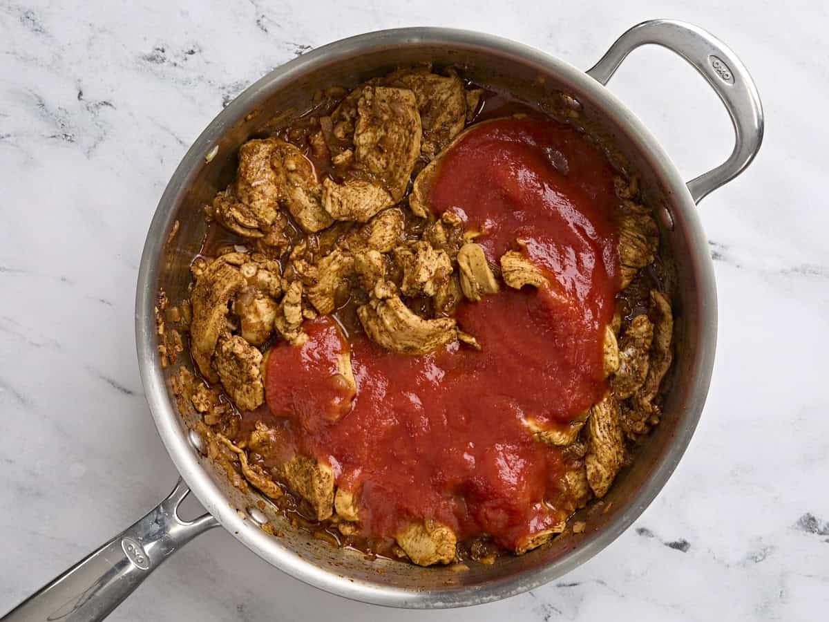 La salsa de tomate enlatada se agregó a una sartén con el relleno de Chimichangas de pollo al horno.