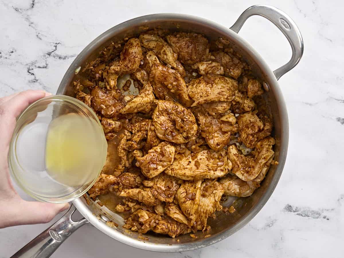 El caldo que se vierte en pollo cocido en una sartén salteada para hacer chimichnagas de pollo al horno.