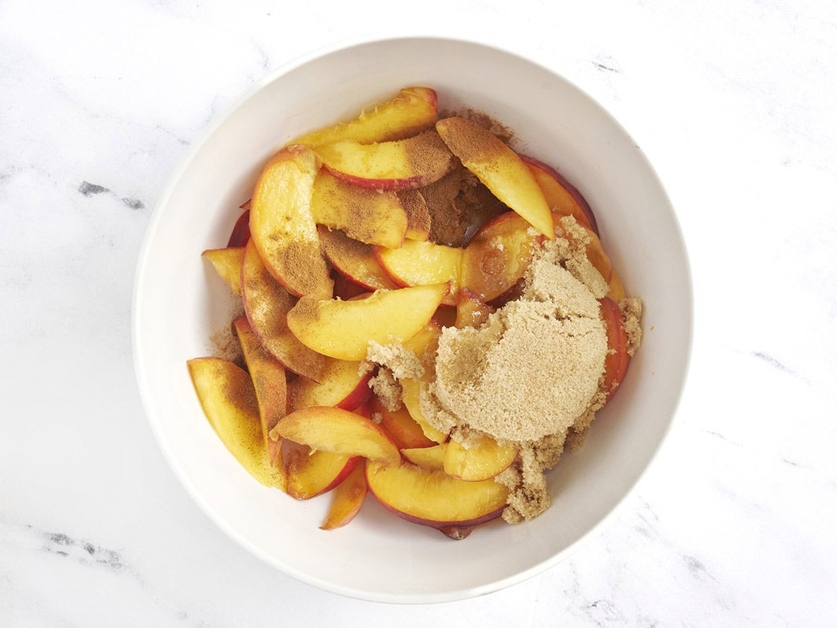 El azúcar moreno y la canela se agregaron a los duraznos frescos en un tazón.