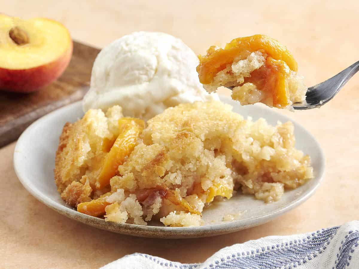 Vista lateral de un plato de zapatero de durazno con una bola de helado de vainilla.