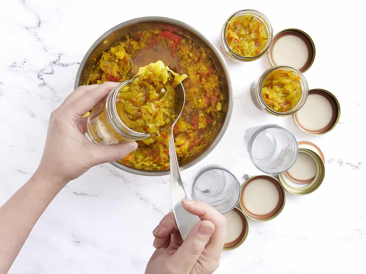 Una mano con cuchara de calabacín casera disfruta en los frascos de enlatado.