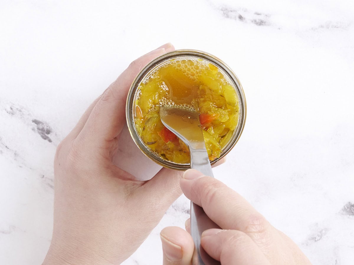 Un tenedor que empuja por el calabacín de sabor en un frasco para que el líquido suba a la parte superior.