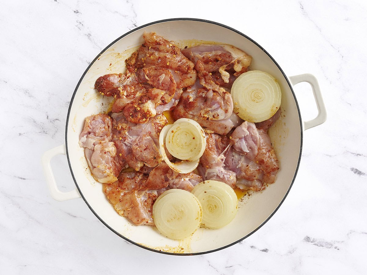 Los muslos de pollo sazonados se agregaron a las mitades de cebolla dorada en una sartén.