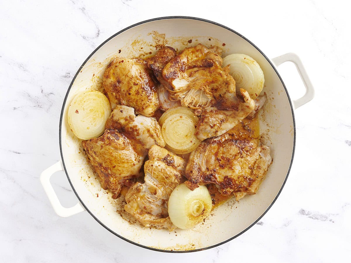 Los muslos de pollo dorados y las mitades de cebolla en una sartén.