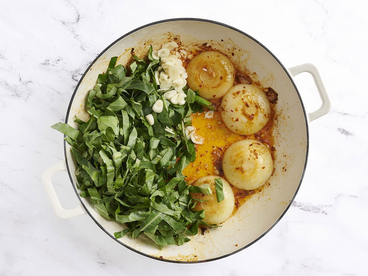 Collard Greens y ajo picado agregado a las mitades de cebolla dorada en una sartén.