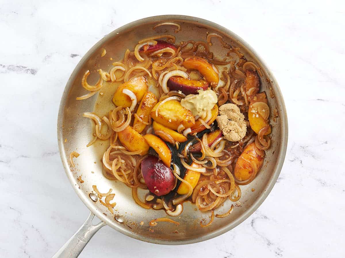 El vinagre balsámico, el dijón y el azúcar moreno se agregaron a una sartén con rodajas de durazno cocidas y cebollas.