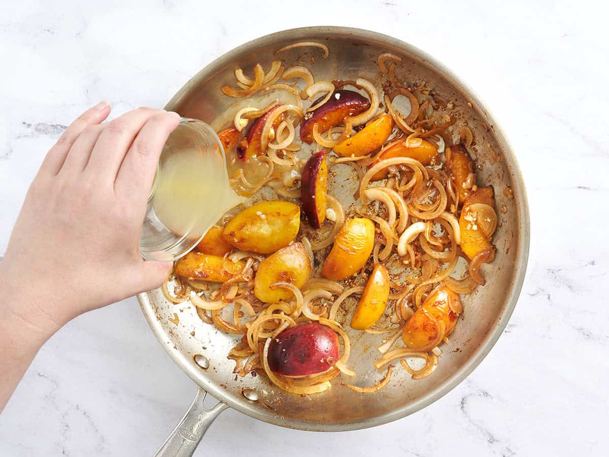 Caldo de pollo desglasando la sartén con duraznos y cebollas para hacer una salsa.