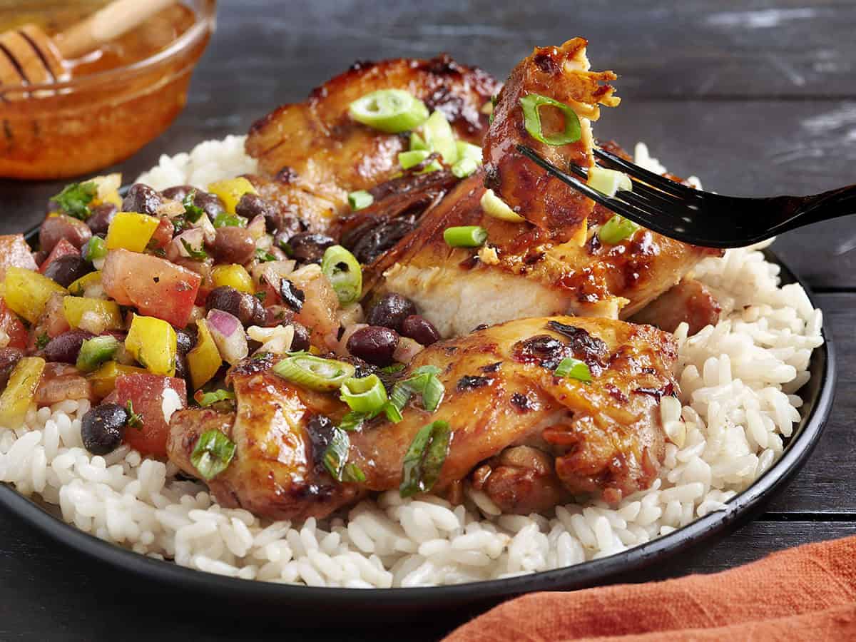 Vista lateral del pollo con miel chipotle en un plato con caviar de vaquero y arroz blanco.