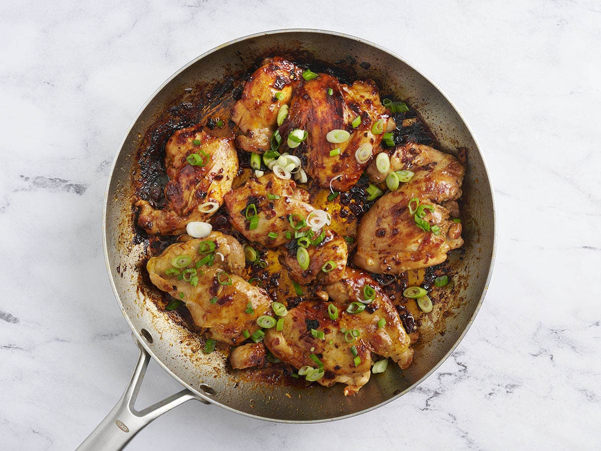 Pollo con miel chipotle terminado en una sartén cubierta de cebollas verdes.