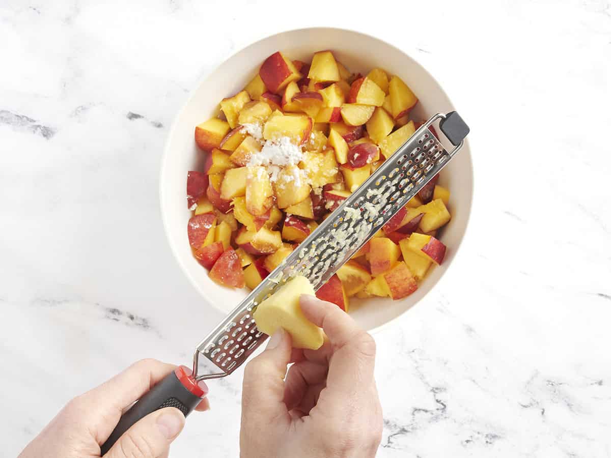 El jengibre se ralló en un tazón de rodajas de durazno y almidón de maíz.