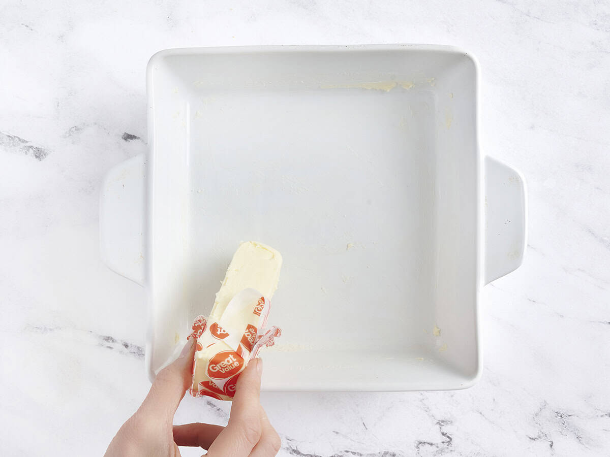 Manos con un palo de mantequilla para engrasar una fuente para hornear.