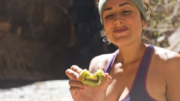 mujer sana camina y comiendo kiwi