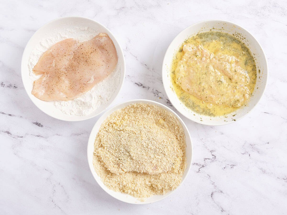 Las chuletas de pechuga de pollo se sumergen en harina, luego huevo y luego migas de pan en tres tazones separados.