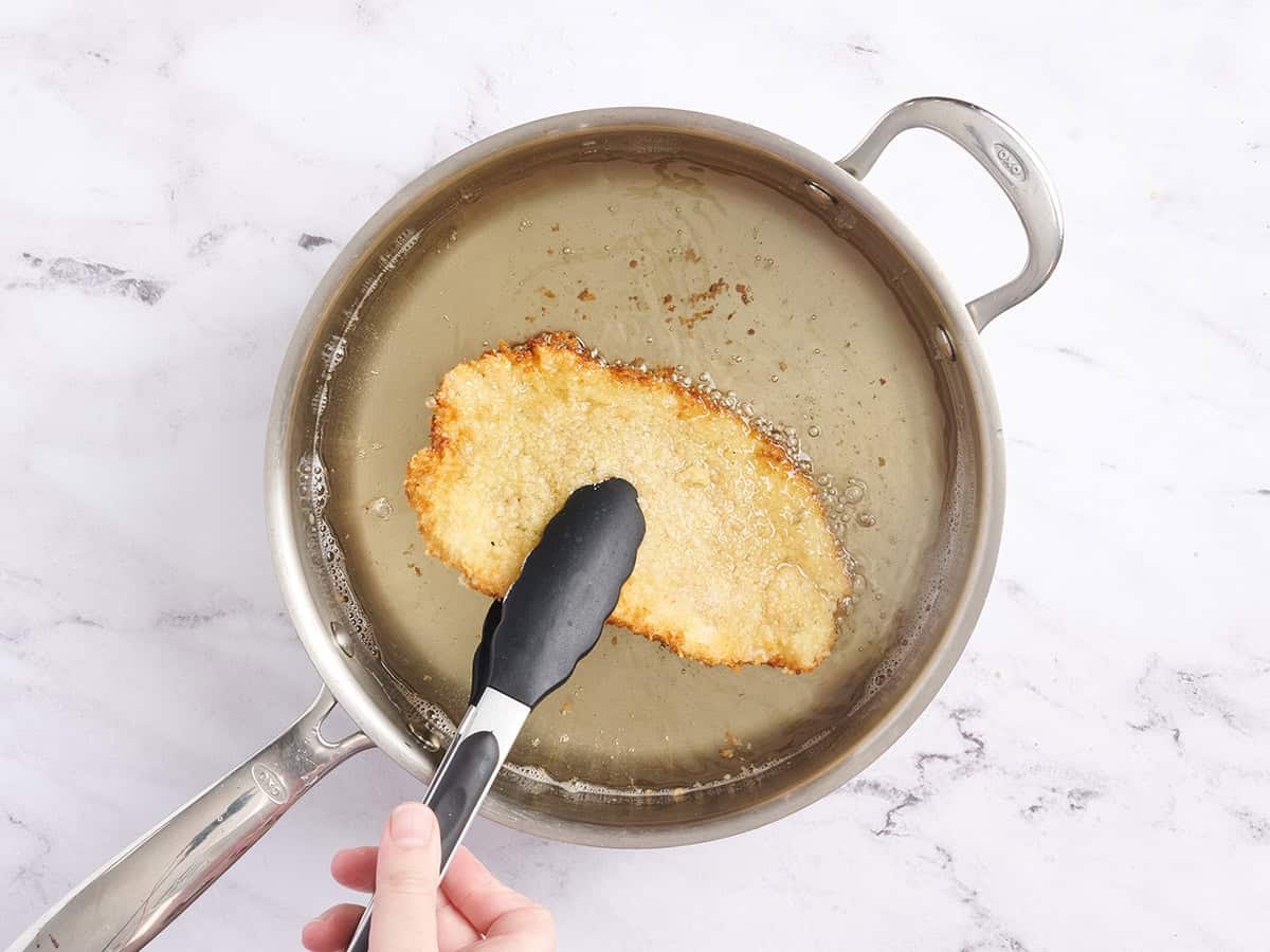 Pintas de pollo volteando un schnitzel de pollo empanado en aceite caliente.