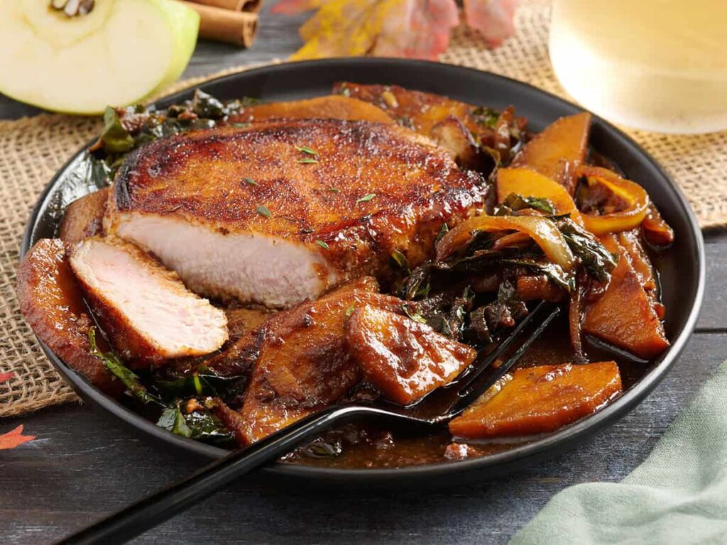 Side view of a plate of an apple butter pork chop, with a slice missing from the pork chop.
