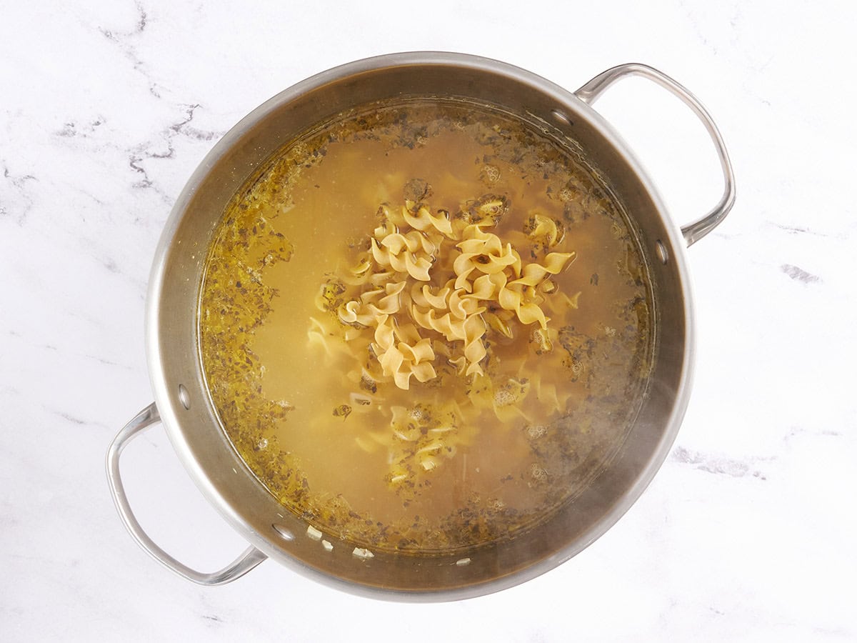 Fideos de huevo crudo agregados a la sopa de fideos de pollo en una olla de sopa.
