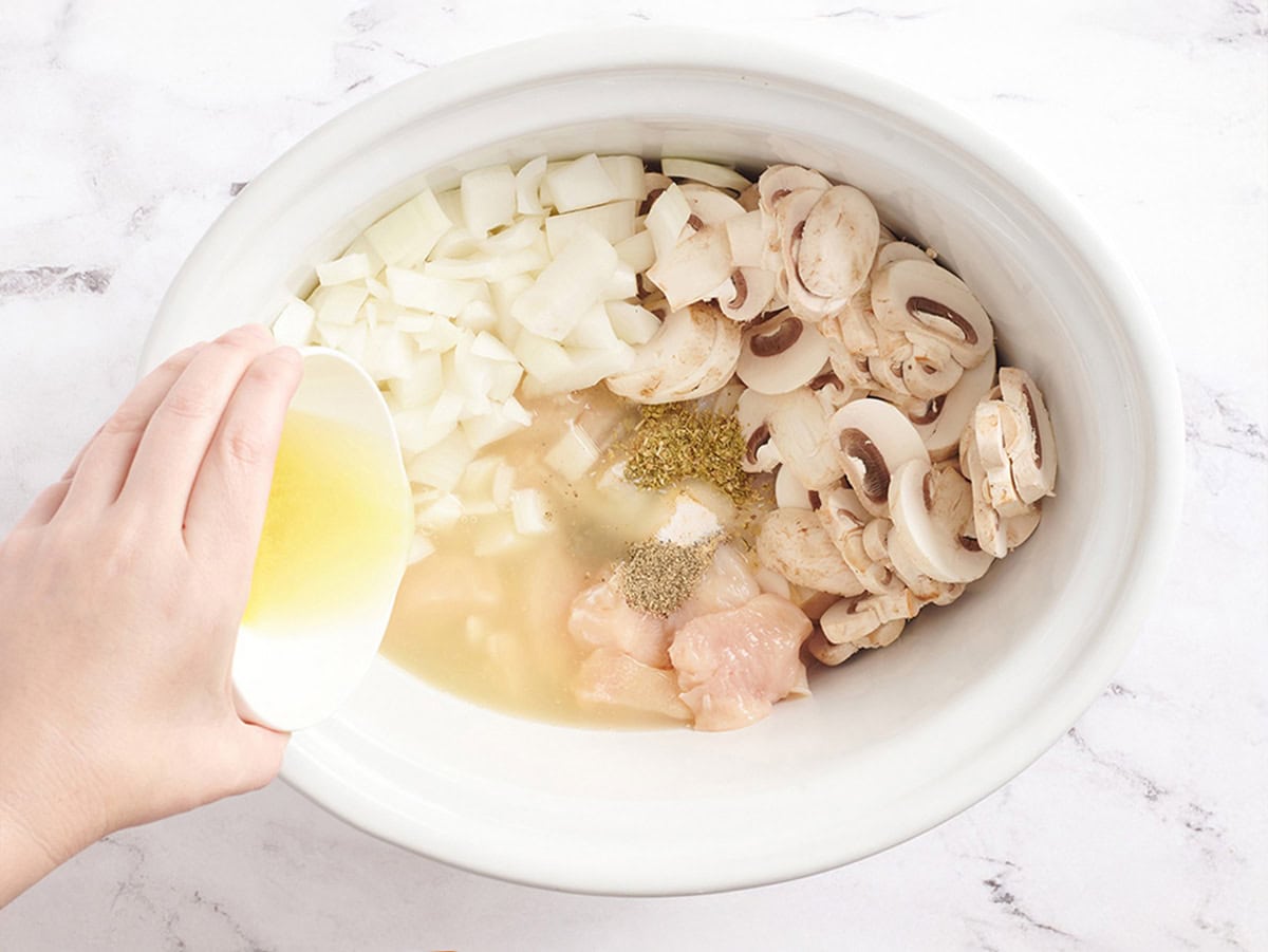 Pollo en cubos, cebolla, champiñones, condimentos y caldo de pollo en una olla de cocción lenta.