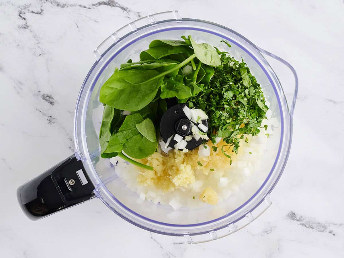 Espinacas, cebolla, ajo y jengibre en un procesador de alimentos.