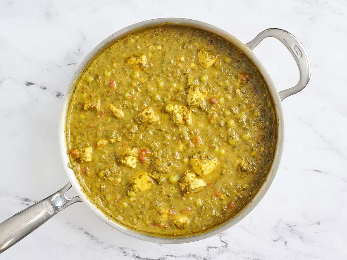 Tofu terminado, espinacas y curry de guisantes verdes en una sartén.