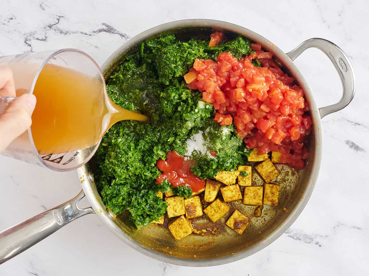 Los tomates cortados en cubitos, el caldo y la pasta de espinacas se agregaron a una sartén con tofu.