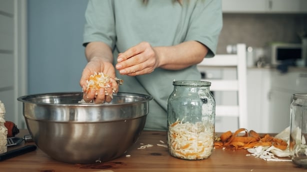 La mujer prepara repollo blanco en escabeche, transfiere el repollo de un tazón de metal a un frasco. Producto fermentado