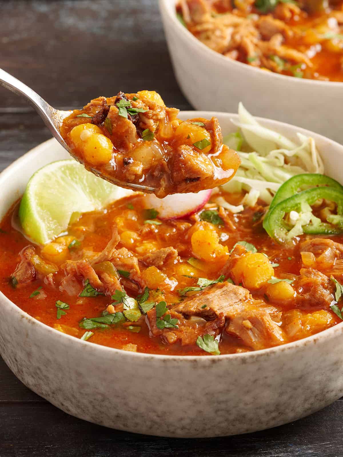 Vista lateral de un plato de posole de 30 minutos con una cuchara tomando un poco del plato.