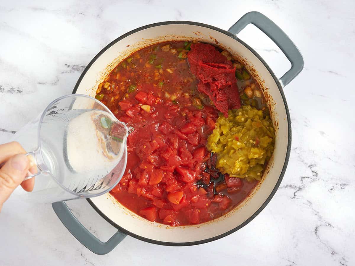 Se agregan ingredientes para chili vegetariano a una olla mientras alguien vierte agua