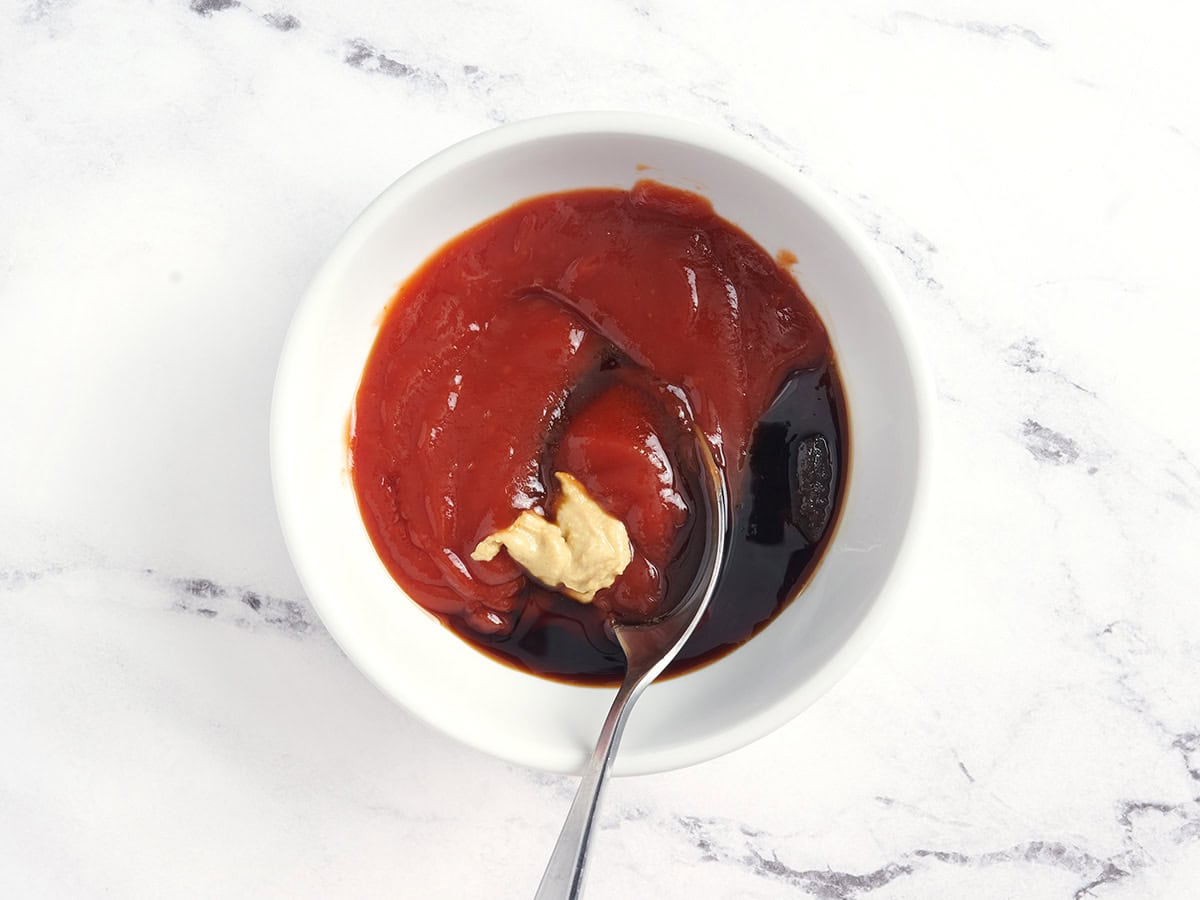 Se mezclan la mostaza Dijon, el ketchup, la salsa de soja y el azúcar moreno con una cuchara en un bol.