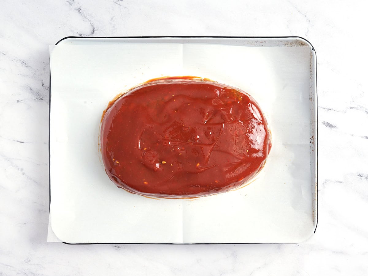 Un pastel de carne de lentejas sobre una bandeja para hornear forrada con papel pergamino y cubierta con glaseado.