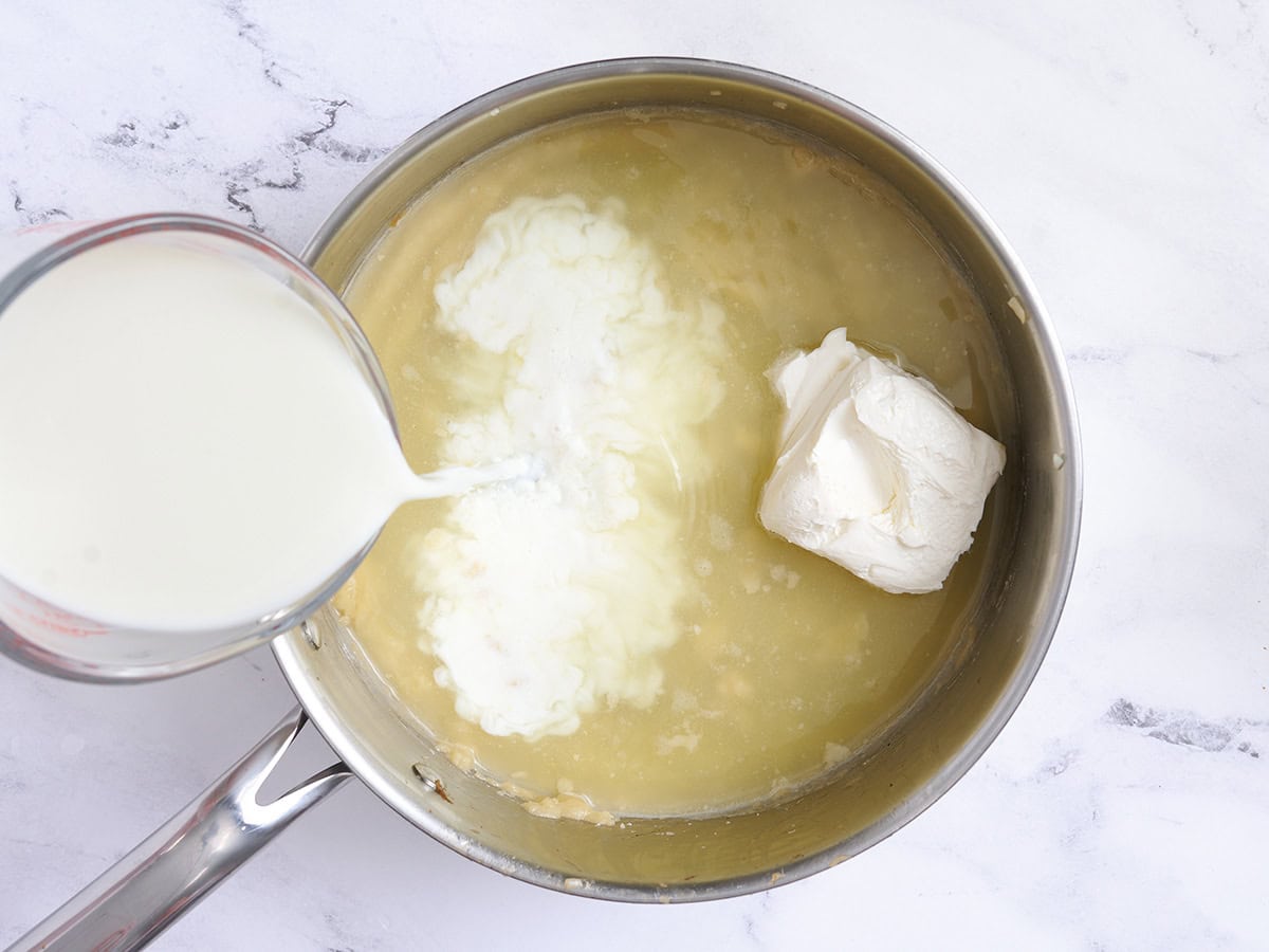 Leche, caldo y queso crema añadidos a un roux en una sartén.