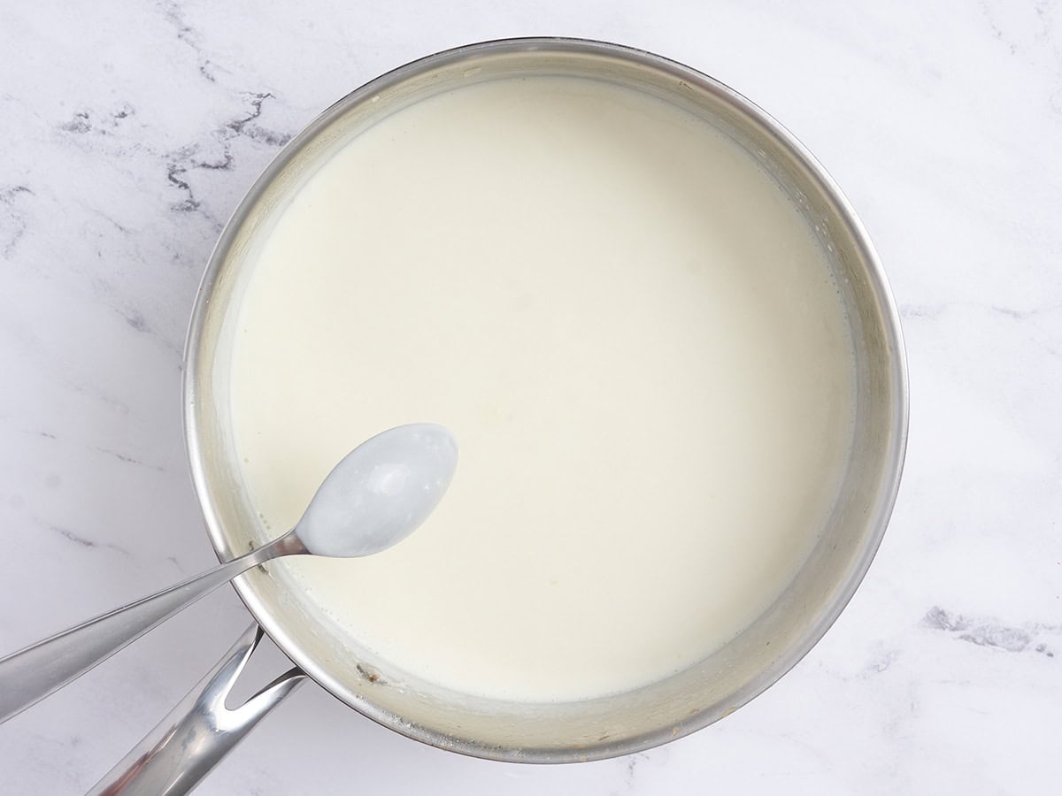 Una cuchara comprobando la consistencia de la salsa espesa en una sartén.