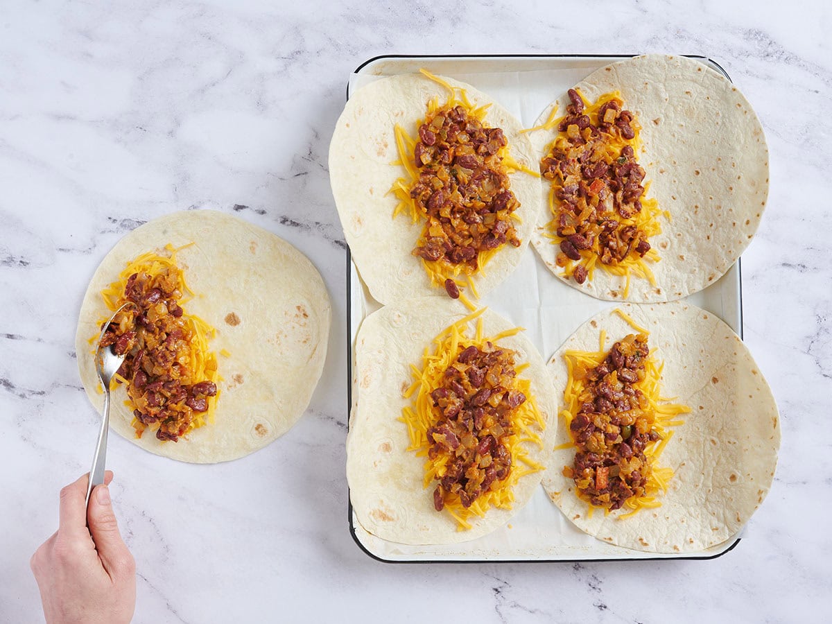 Tortillas de harina cubiertas con queso cheddar rallado y frijoles.