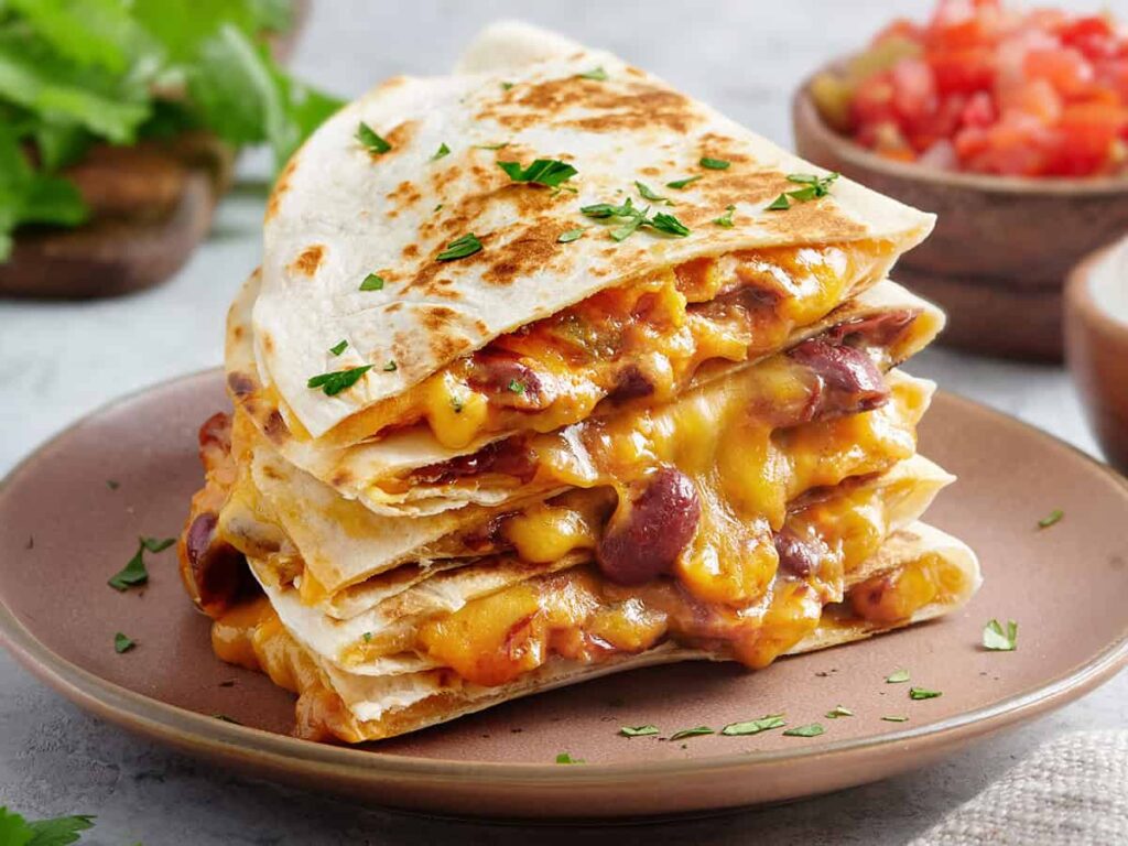 Side view of a stack of cheesy kidney bean quesadillas on a plate.