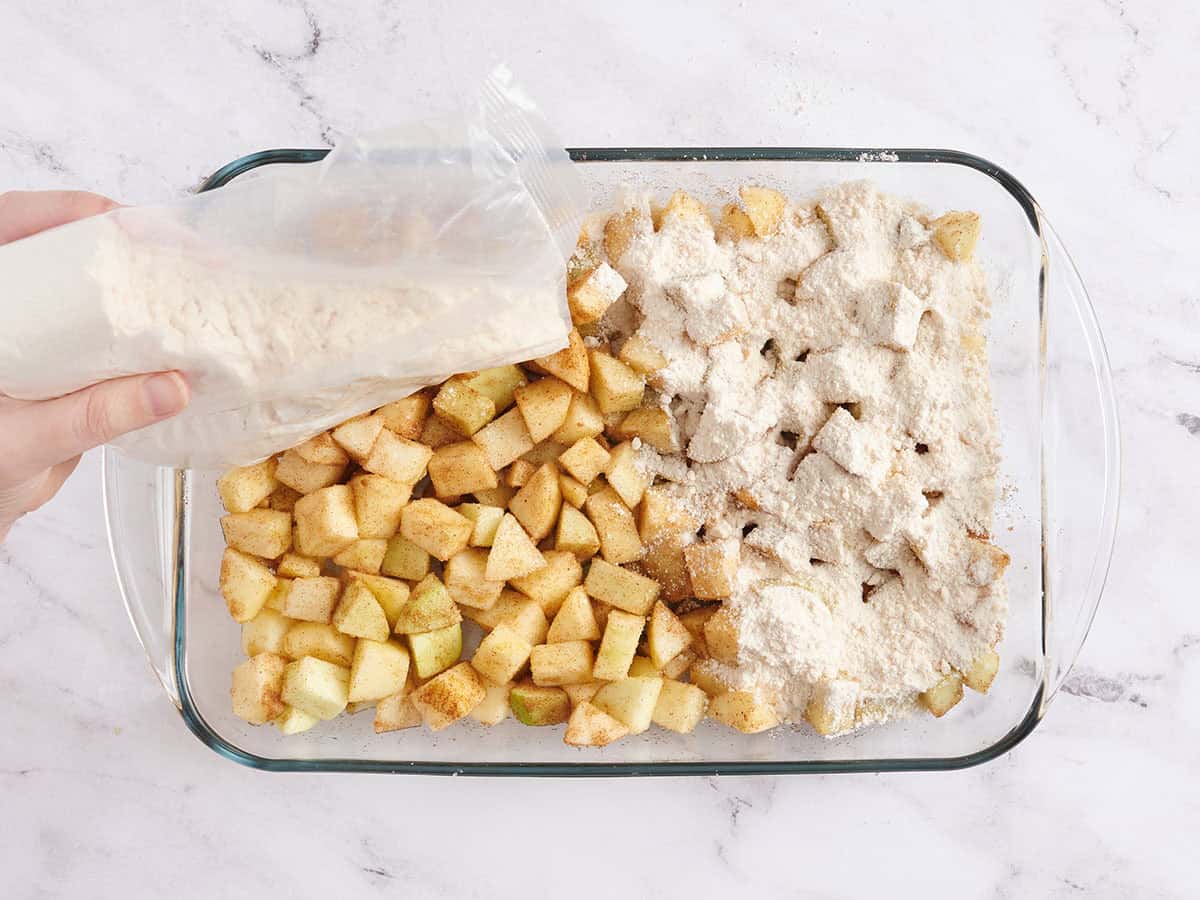 Se espolvorea la mezcla para pastel sobre las manzanas sazonadas en una fuente para horno.