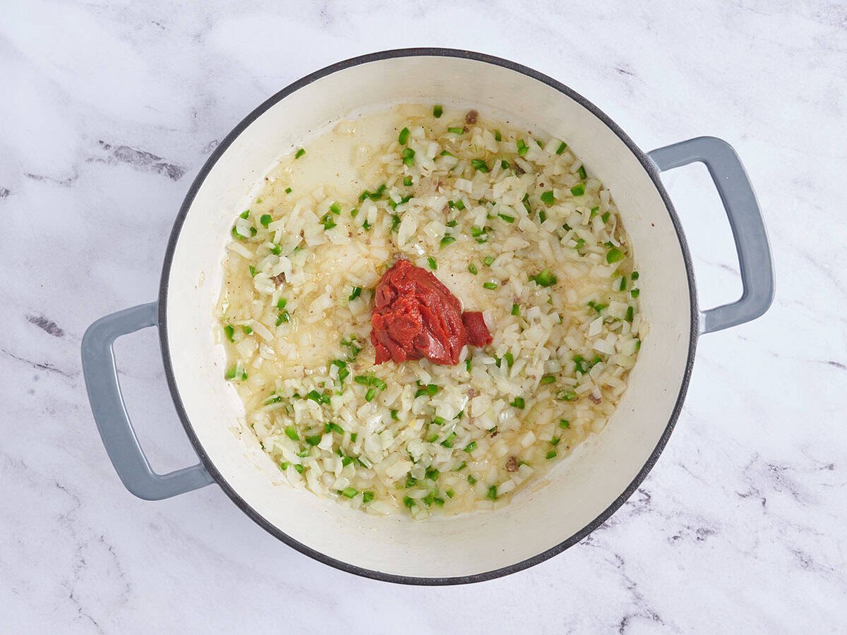 Pasta de tomate agregada a cebollas salteadas y jalapeños en una olla.