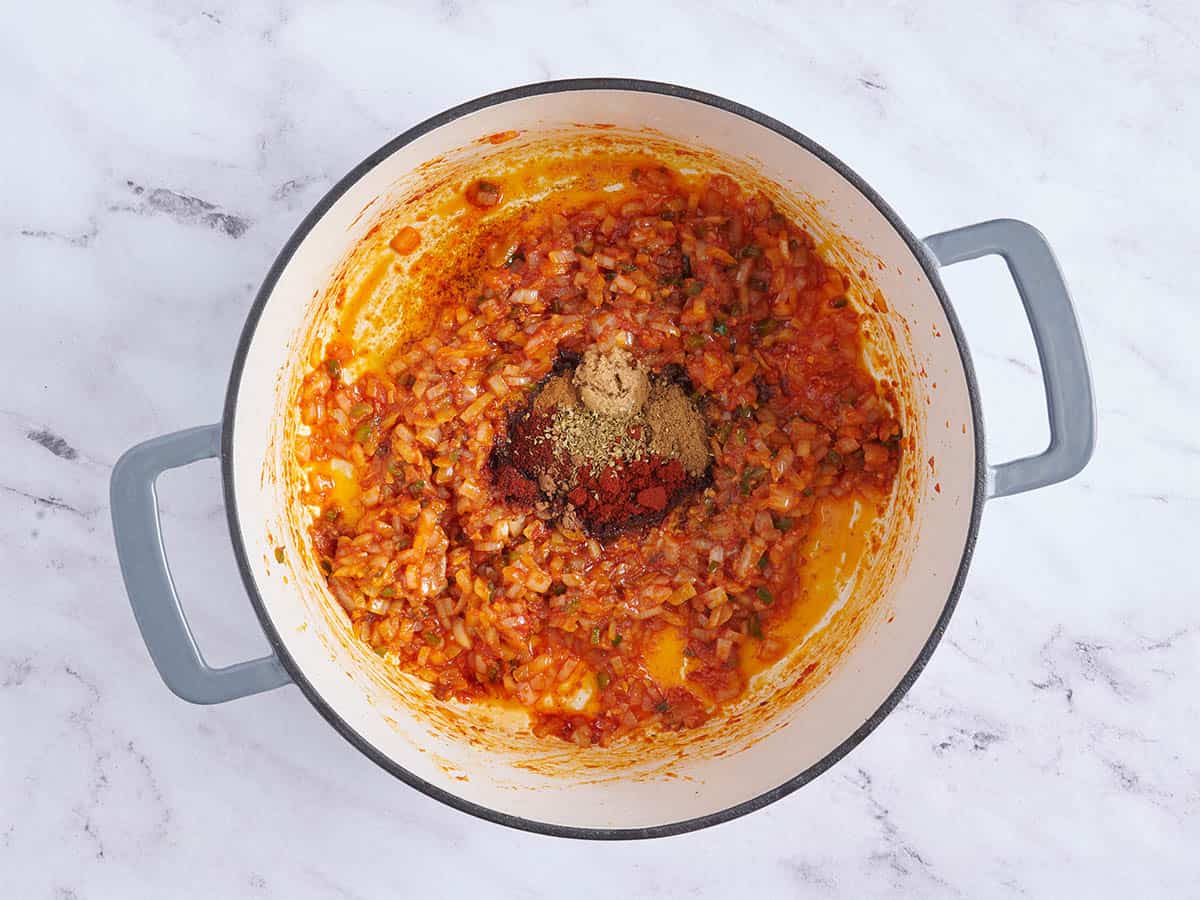 Se agregan condimentos a la pasta de tomate y la cebolla en una olla para hacer chile de Texas.