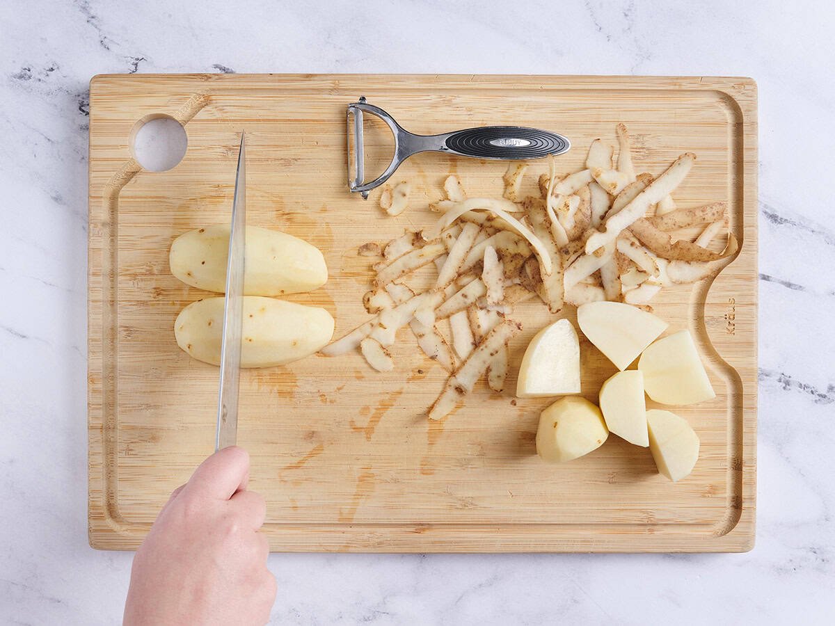 Patatas peladas sobre una tabla de cortar de madera cortadas con un cuchillo.