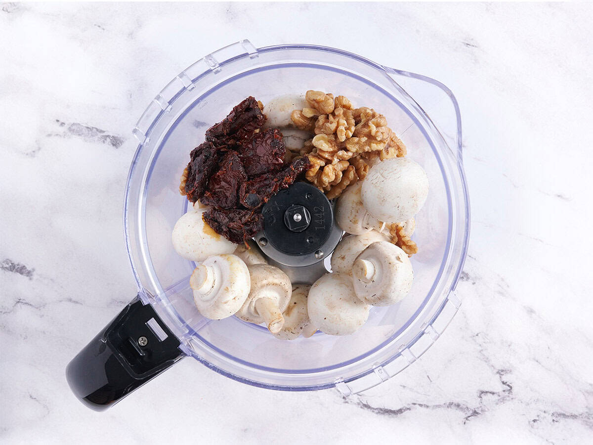 Tomates, champiñones y nueces secos en un procesador de alimentos.