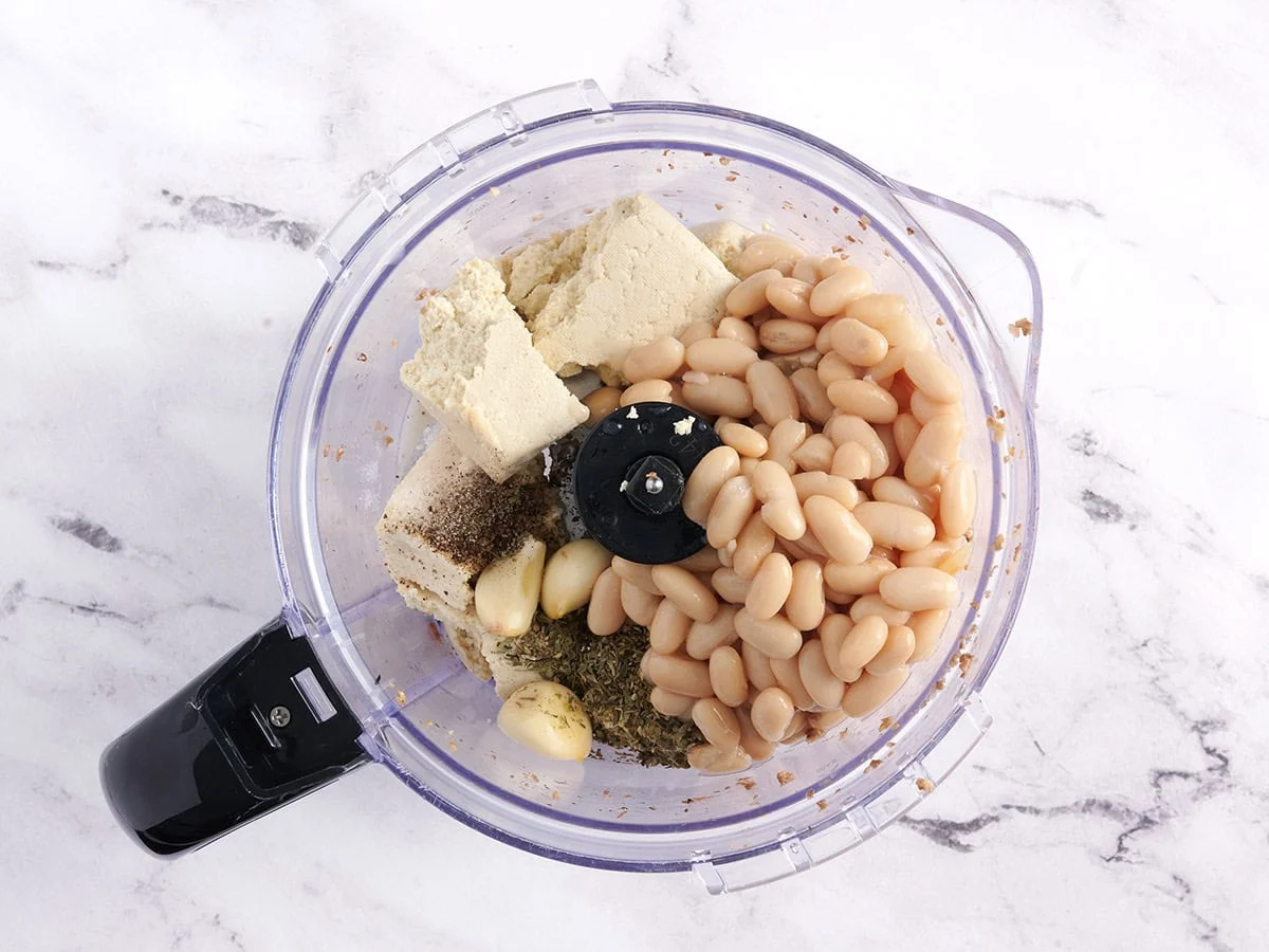 Tofu, frijoles blancos y condimentos en un procesador de alimentos.