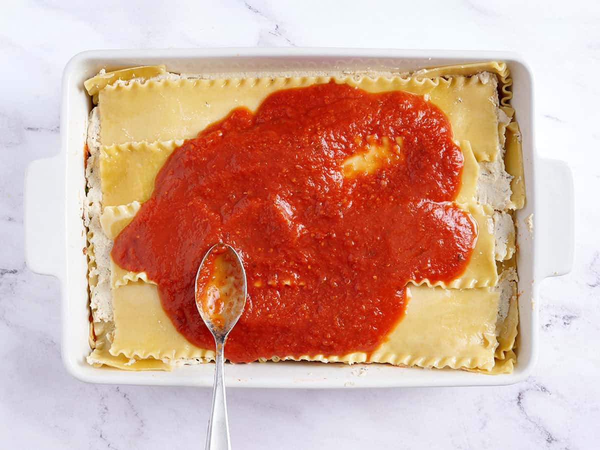 Salsa marinara agregada a lasaña vegana.