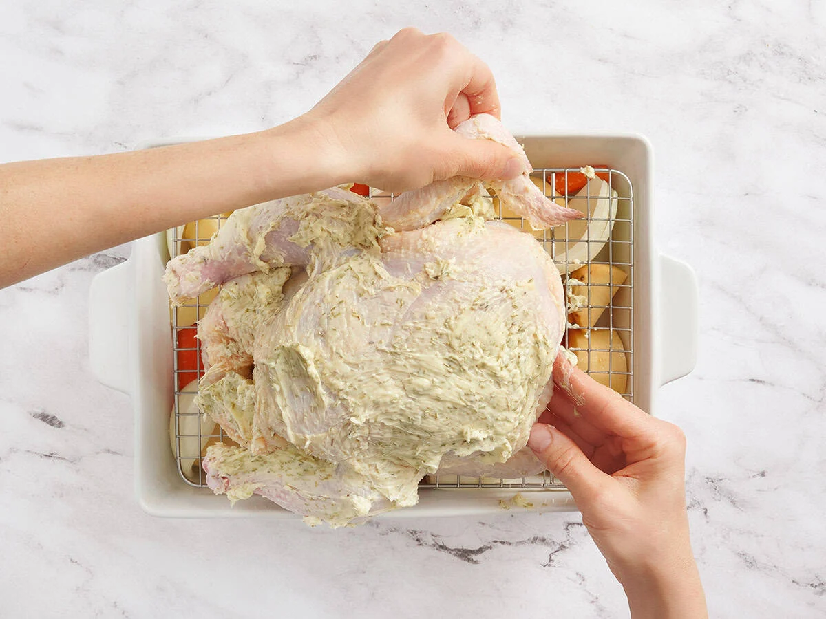 Manos metiendo alitas de pollo debajo de un pollo entero.