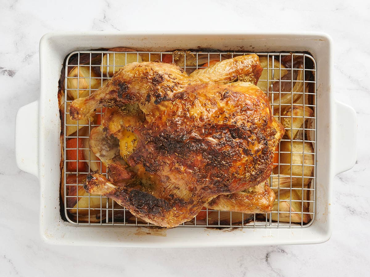 Pollo asado en una fuente para horno sobre verduras.
