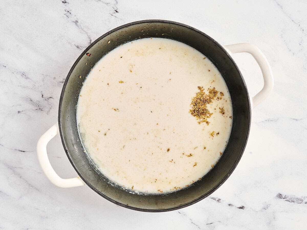 Se añaden condimentos, caldo y especias a una sartén para hacer una salsa de crema.