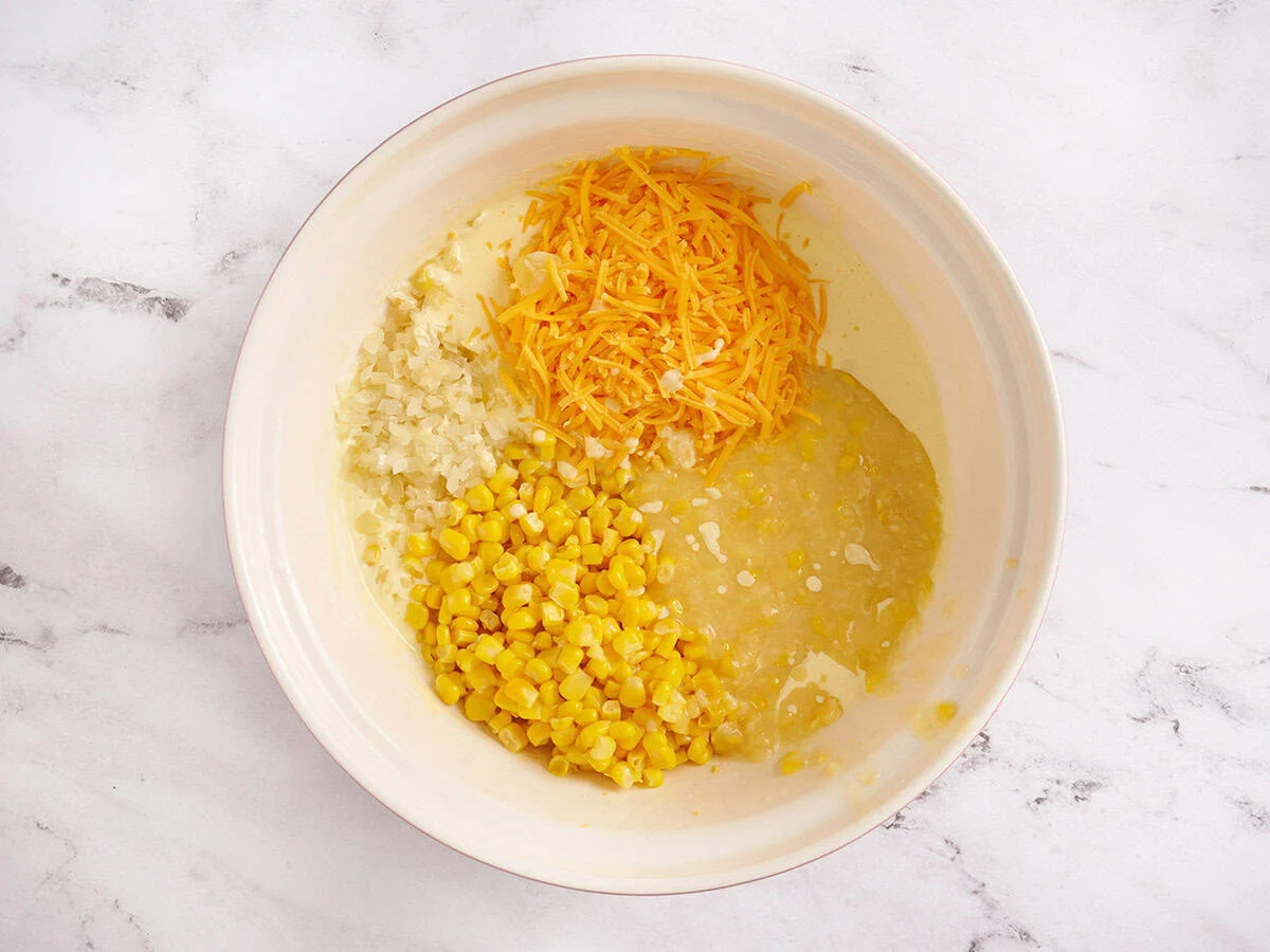 Agregar maíz, queso y cebolla enlatados al tazón de yogur/huevos.  