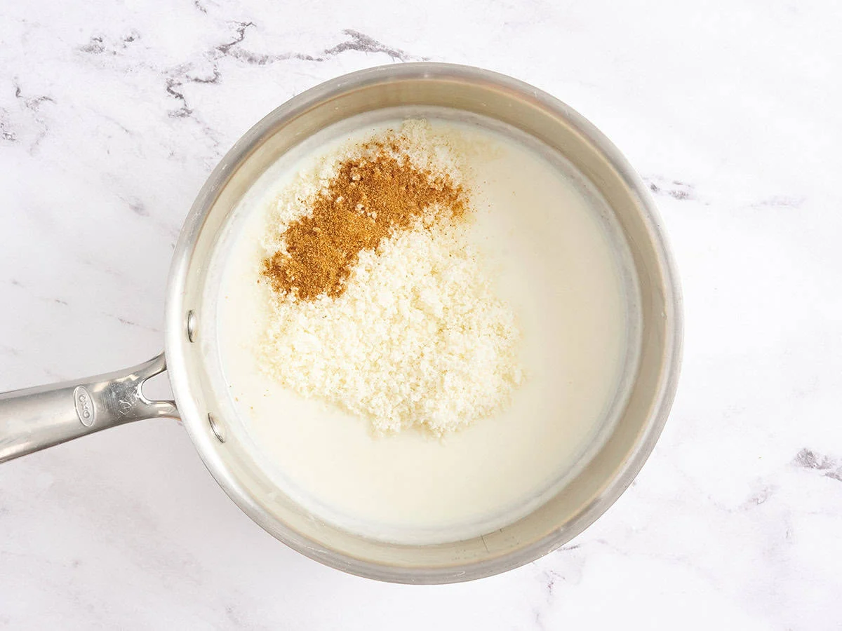 Parmesano y condimentos en salsa de crema blanca en una cacerola.