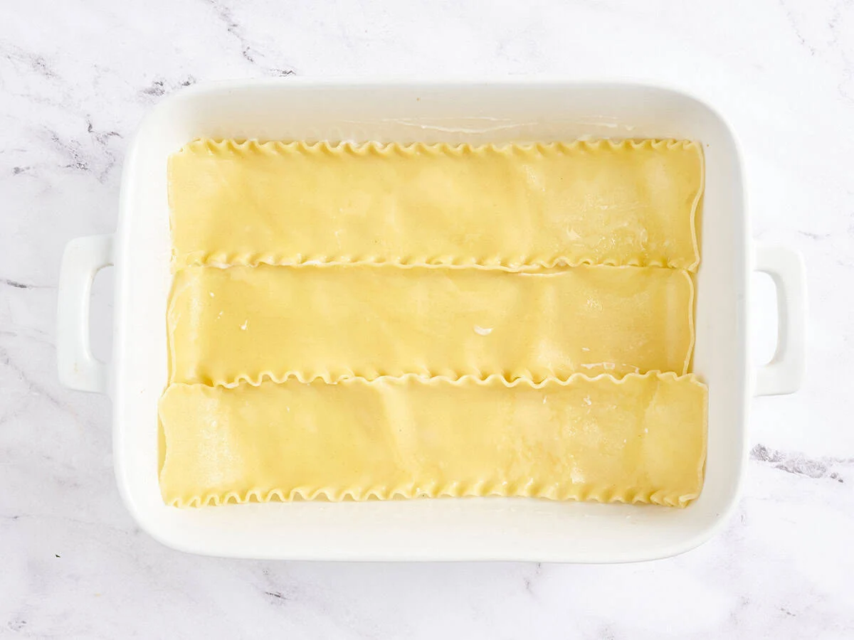 Fideos de lasaña cocidos añadidos a una fuente para horno.