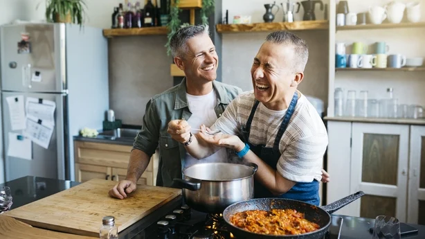 Una alegre pareja gay adulta hablando y divirtiéndose mientras cocina en una cocina