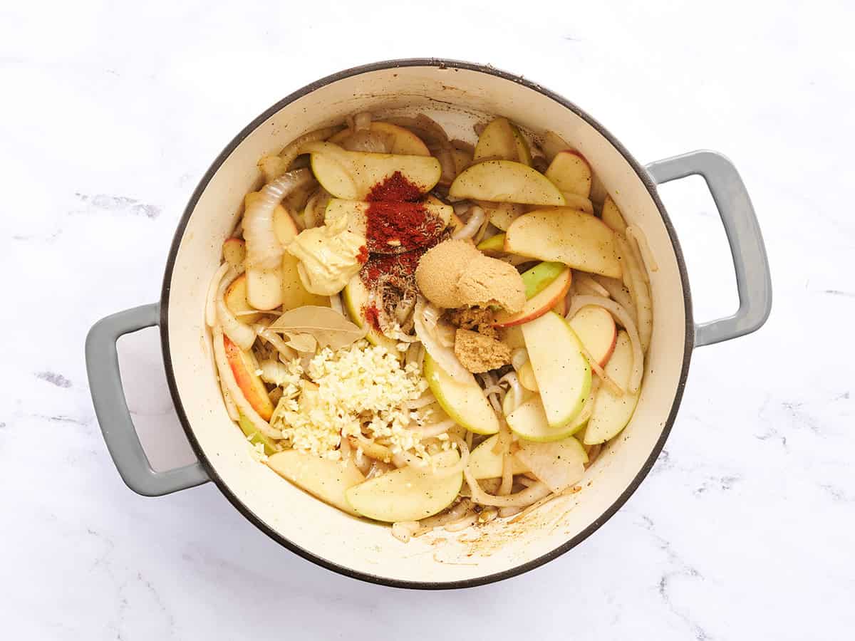 Especias agregadas a una olla holandesa de cebollas y manzanas.