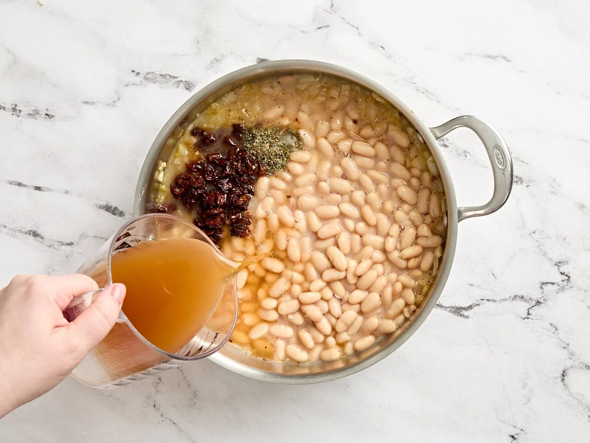 Se añaden especias y caldo a los frijoles blancos en una sartén.