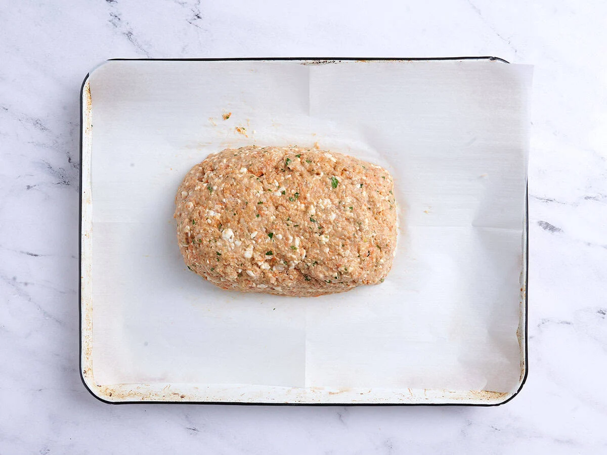 Pastel de carne de pollo con forma de hogaza sobre una bandeja para hornear forrada con papel pergamino. 